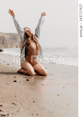 Woman beach happiness kneeling on the sandy shore with arms raised towards the sky during a sunny day by the sea Woman beach happiness kneeling on the sandy shore with arms raised towards the sky during a sunny day by the sea 143717427