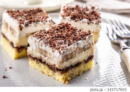 Delicious layered cakes with cream, bananas, and fluffy whipped cream served on an elegant plate. The top of the desserts is sprinkled with finely grated dark chocolate Delicious layered cakes with cream, bananas, and fluffy whipped cream served on an elegant plate. The top of the desserts is sprinkled with finely grated dark chocolate 143717603