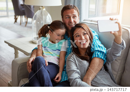 Interracial parents, girl and selfie on couch for smile, hug and relax with care, mobile app or memory in home. Father, mother and daughter with embrace, social media or love on sofa in family house 143717717