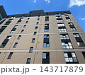 A low angle view shows a multi-story apartment building with rows of windows in a city under a blue sky during the day 143717879