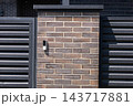 A building intercom is mounted on a brick pillar between metal gates at an entrance in daylight 143717881