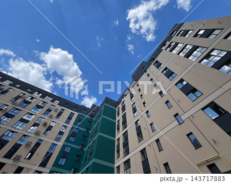 New development apartment buildings rise around an inner courtyard in a city, viewed from below during the day under a blue sky 143717883