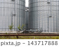 Two grain storage silos rise above tracks at an agricultural facility during the day, with no workers or rail activity visible 143717888