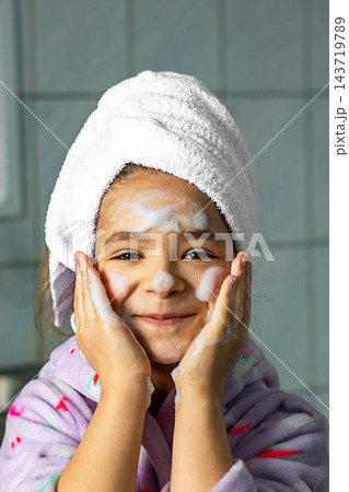 Little girl washing her face with foam and towel wrapped after bath, smiling in bathroom Little girl washing her face with foam and towel wrapped after bath, smiling in bathroom 143719789