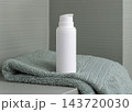 White cosmetic borttle mockup on light green towel in bathroom, unbranded packaging 143720030