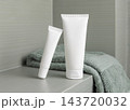 White cream tubes mockup near green terry towel in bathroom closeup, unbranded cosmetic packaging 143720032