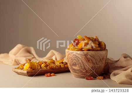 Yellow sultana raisins in a wooden bowl on a beige background. 143723328