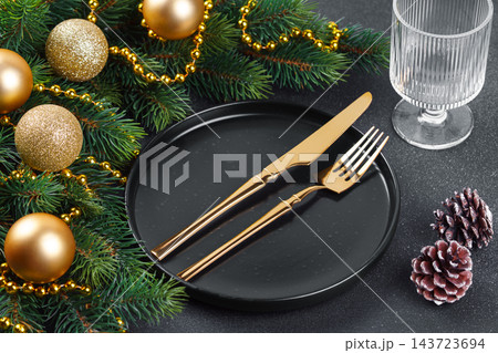 Elegant Christmas table setting with gold cutlery on black plate and decorated spruce branches Elegant Christmas table setting with gold cutlery on black plate and decorated spruce branches 143723694