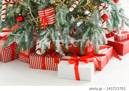 Red wrapped gift boxes, presents under festive Christmas tree with lights and holiday decorations 143723701