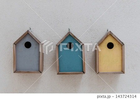 Three Colorful Wooden Birdhouses Hanging on a White Wall 143724314