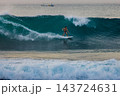 Surfer man crouching low on a white surfboard while carving through a deep blue wave with ocean spray 143724631