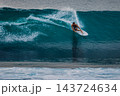 Surfer man riding on surfboard while and carving through a blue wave with water spray 143724634