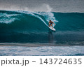 Surfer man riding on surfboard while and carving through a blue wave with water spray 143724635