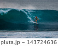 Surfer man riding on surfboard while and carving through a blue wave with water spray 143724636