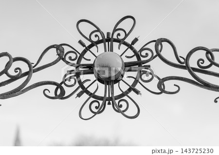 A detailed close-up view of an ornate metal gate with circular design featuring eight flowing arms and a central light fixture or reflective surface A detailed close-up view of an ornate metal gate with circular design featuring eight flowing arms and a central light fixture or reflective surface 143725230