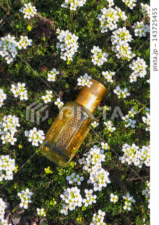 Exotic Perfume Oil Bottle Lying in a Field of Small White Flowers Exotic Perfume Oil Bottle Lying in a Field of Small White Flowers 143725455
