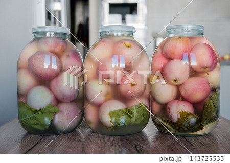 Three large glass jars with fermented pickled apples and green leaves on wooden table, traditional winter food preservation Three large glass jars with fermented pickled apples and green leaves on wooden table, traditional winter food preservation 143725533