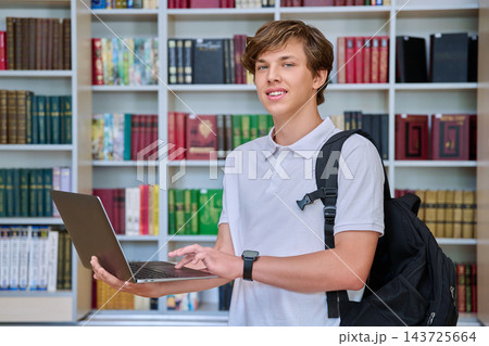 Teenage boy student using laptop with backpack in library portrait 143725664