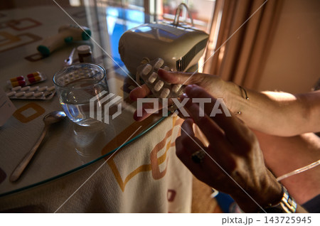Woman preparing medication with nebulizer and pills at home beside glass of water Woman preparing medication with nebulizer and pills at home beside glass of water 143725945