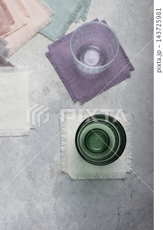 Glass cups on pastel fringed linen coasters set Glass cups on pastel fringed linen coasters set 143725981