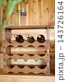 Three wine bottles rest in a wooden rack against a wood wall, with a plant beside them indoors during the day 143726164