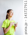 Young girl in green shirt holding a glass of water with a grateful smile and hand on chest 143727911