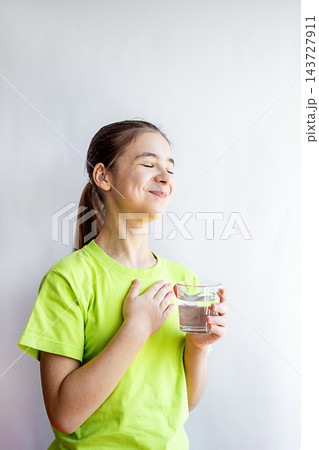 Young girl in green shirt holding a glass of water with a grateful smile and hand on chest Young girl in green shirt holding a glass of water with a grateful smile and hand on chest 143727911