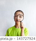 Curious girl examining face with magnifying glass in playful close-up portrait 143727924