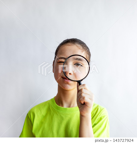 Curious girl examining face with magnifying glass in playful close-up portrait 143727924