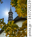 Autumn Church Steeple Framed by Golden Leaves Under Bright Sun and Clear Blue Sky 143728229