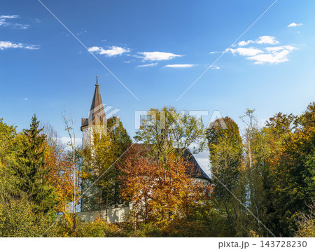 Historic Church Tower Peeking Through Autumn Trees Under A Bright Blue Sky In Rural Landscape 143728230