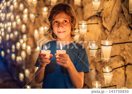 Boy holding votive lights beside a wall of glowing candles. Boy holding votive lights beside a wall of glowing candles. 143730850