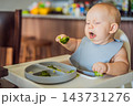 Baby exploring an unfamiliar taste during a broccoli meal. 143731276