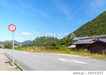 秋晴れの青空と山々の麓を走る道路沿いに立つ交通標識と田舎の風景 143731551