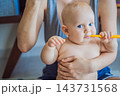 Infant exploring a toothbrush while mother demonstrates toothbrushing. 143731568