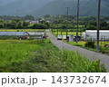 山間に広がる農村の風景とビニールハウス、田畑を通る農道 143732674