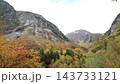 黄色や赤に色づいた木々が埋める谷と、岩肌の山がそびえる秋の山岳風景 143733121