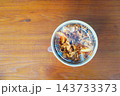 A takeout container of thinly sliced spicy meat and onions over rice, sprinkled with sesame seeds, on a wooden table. Top-down view of a packaged meal for delivery or carry-out. 143733373
