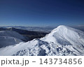 青空の下、雪に覆われた稜線から見下ろす谷と遠くの雪山の連なり 143734856