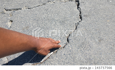 Hand pointing to a crack in a paved surface outdoors 143737566