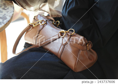 Woman carrying a brown leather handbag on her lap indoors 143737606