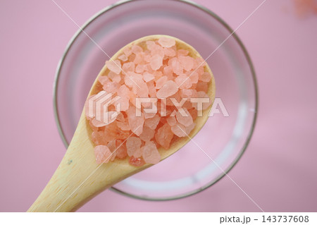 Wooden spoon holding pink salt crystals over a glass of water Wooden spoon holding pink salt crystals over a glass of water 143737608