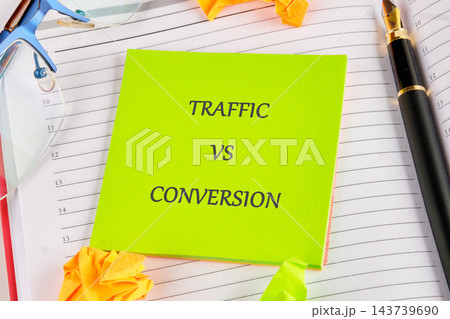 A green note marked traffic versus conversion rests on an open planner with a pen, glasses, and paper clips on a desk 143739690