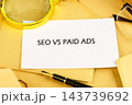 A paper sheet labeled SEO vs paid ads lies on a desk with a pen, glasses, and magnifying glass during a marketing work session 143739692