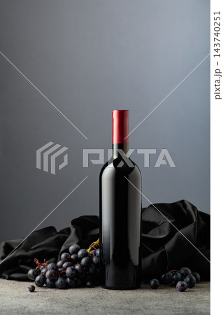 Bottle of red wine with grapes on a grey background. 143740251