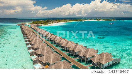 Panoramic overwater villa row stretching vivid turquoise Maldives lagoon jetty wide bright tropical resort. Digital nomad remote workation. Dream office freelance lifestyle Panoramic overwater villa row stretching vivid turquoise Maldives lagoon jetty wide bright tropical resort. Digital nomad remote workation. Dream office freelance lifestyle 143740467