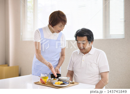 介護施設で食事を提供されるシニア男性とスタッフのシニアの女性 介護施設で食事を提供されるシニア男性とスタッフのシニアの女性 143741849