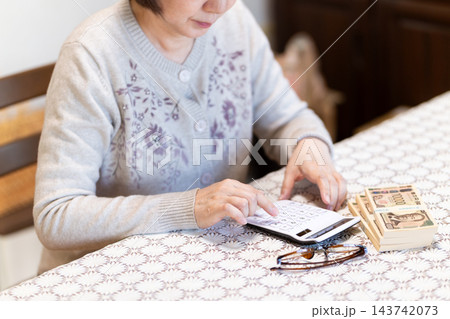 電卓でお金の計算をするミドル・シニア女性 電卓でお金の計算をするミドル・シニア女性 143742073