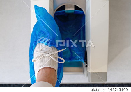 Foot Wearing White Sneaker Enters Blue Automatic Shoe Cover Dispenser Foot Wearing White Sneaker Enters Blue Automatic Shoe Cover Dispenser 143743160