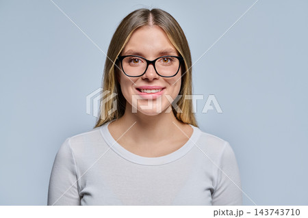 Close-up portrait of smiling young blonde woman in black glasses on grey background 143743710
